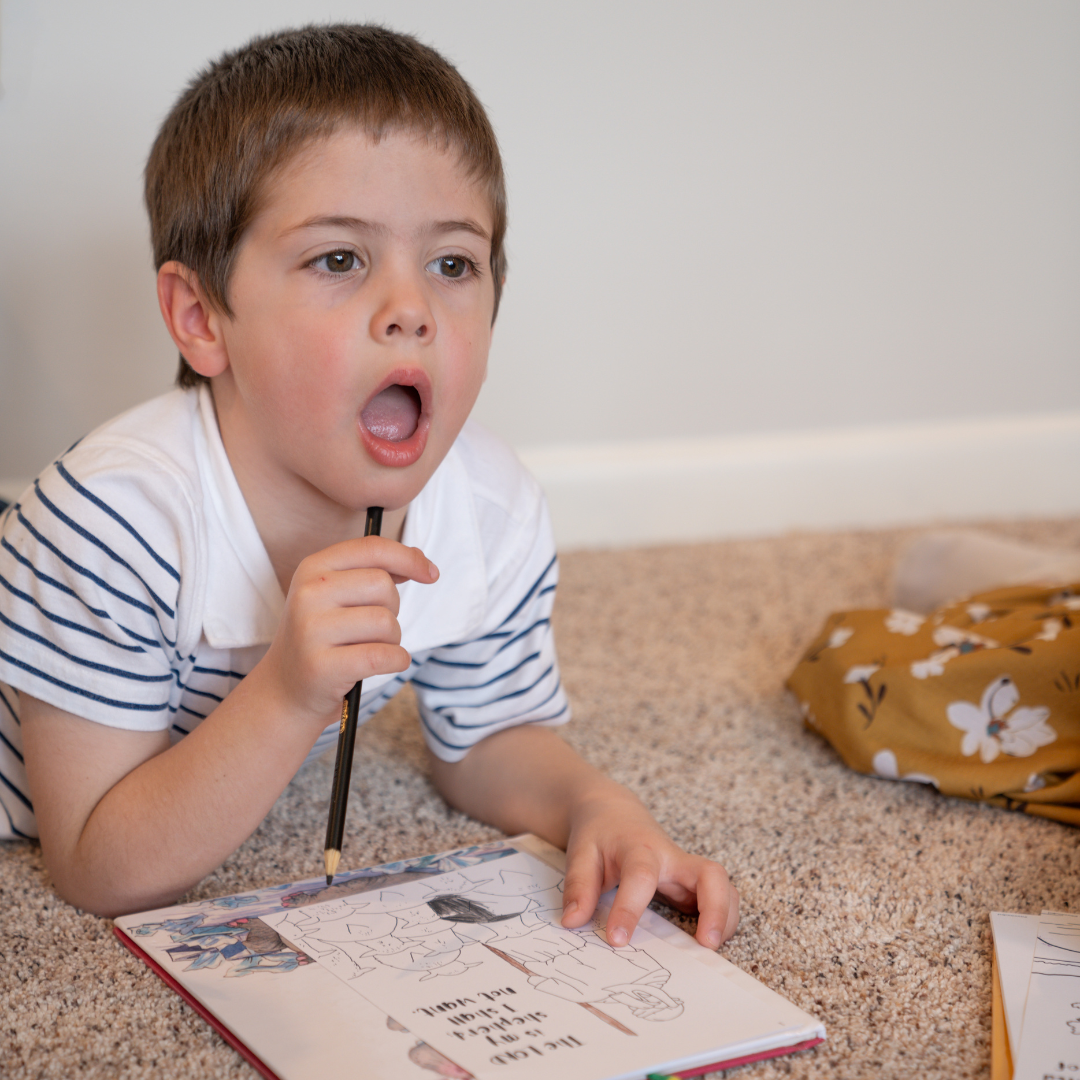 Boy coloring Psalm 23 KJV coloring page while laying on the floor.