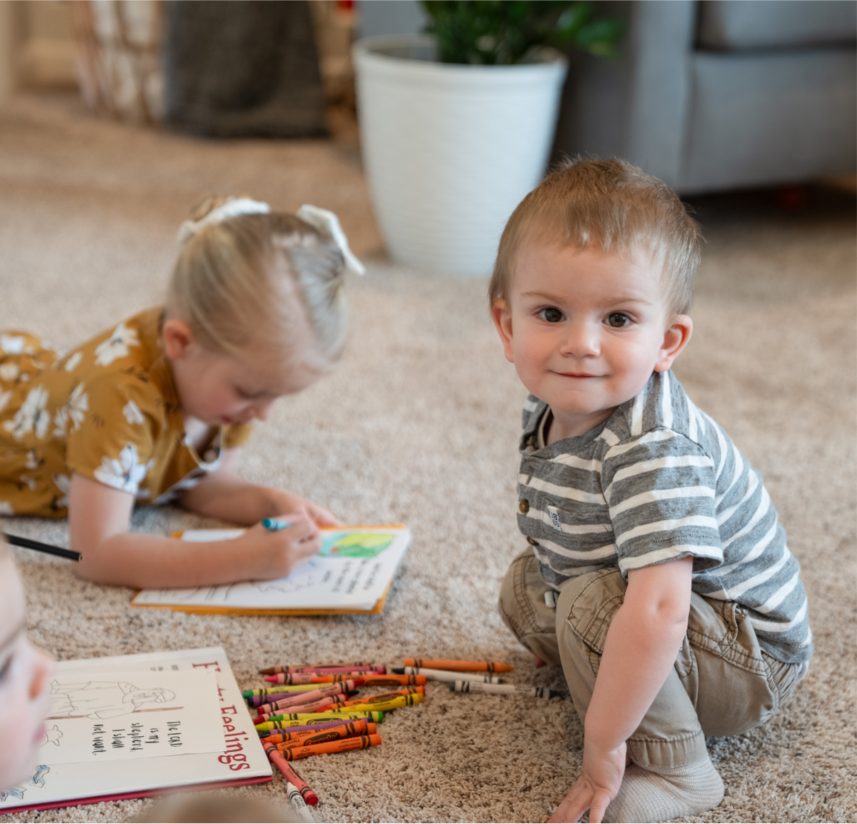 Two children sitting on the carpet with crayons while coloring Bible verse illustrations
