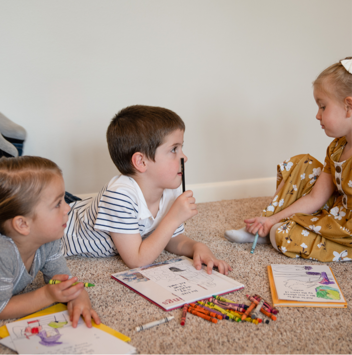 Three children laying on the floor with coloring pages and crayons 