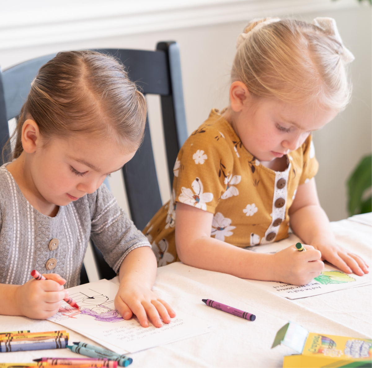 Two Mennonite girls coloring at a table with crayons 